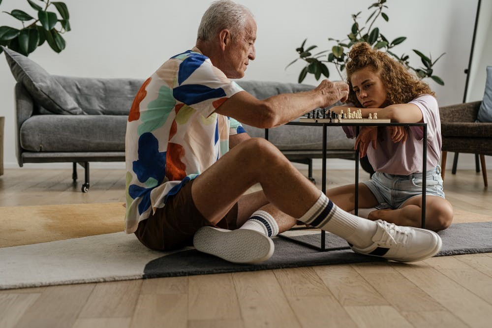 Elderly man and a woman sitting on the carpet while playing chess